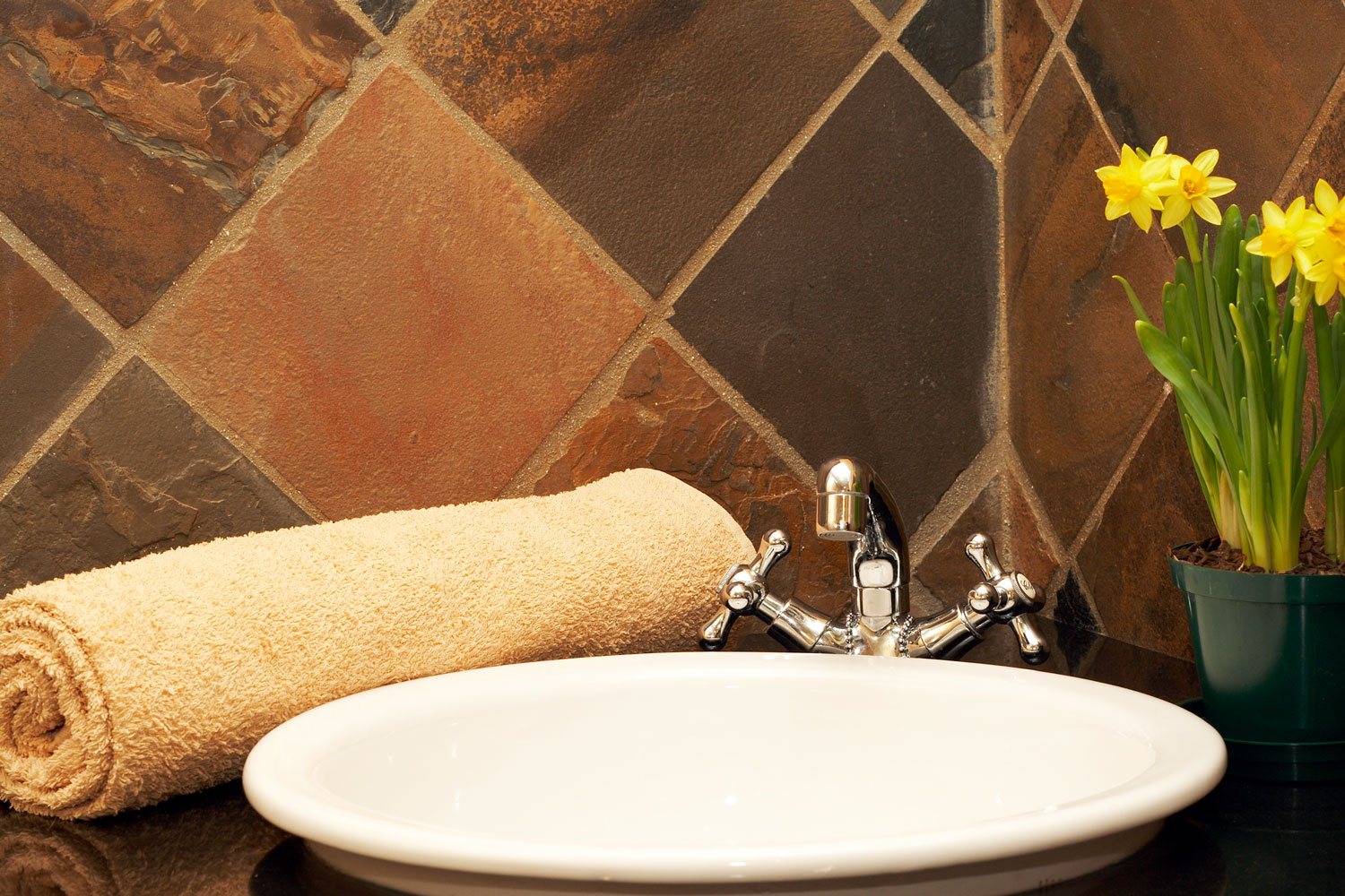 A rolled brown towel on vanity area inside a brown tiled bathroom