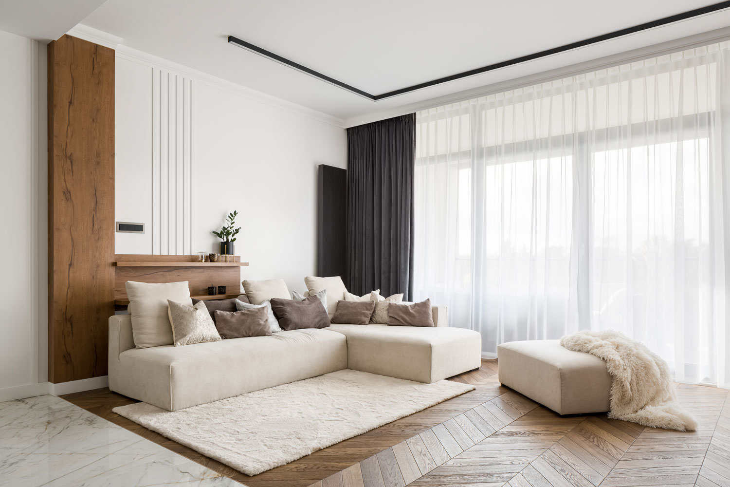 An off white sectional sofa with brown and beige throw pillows and ceiling high curtains