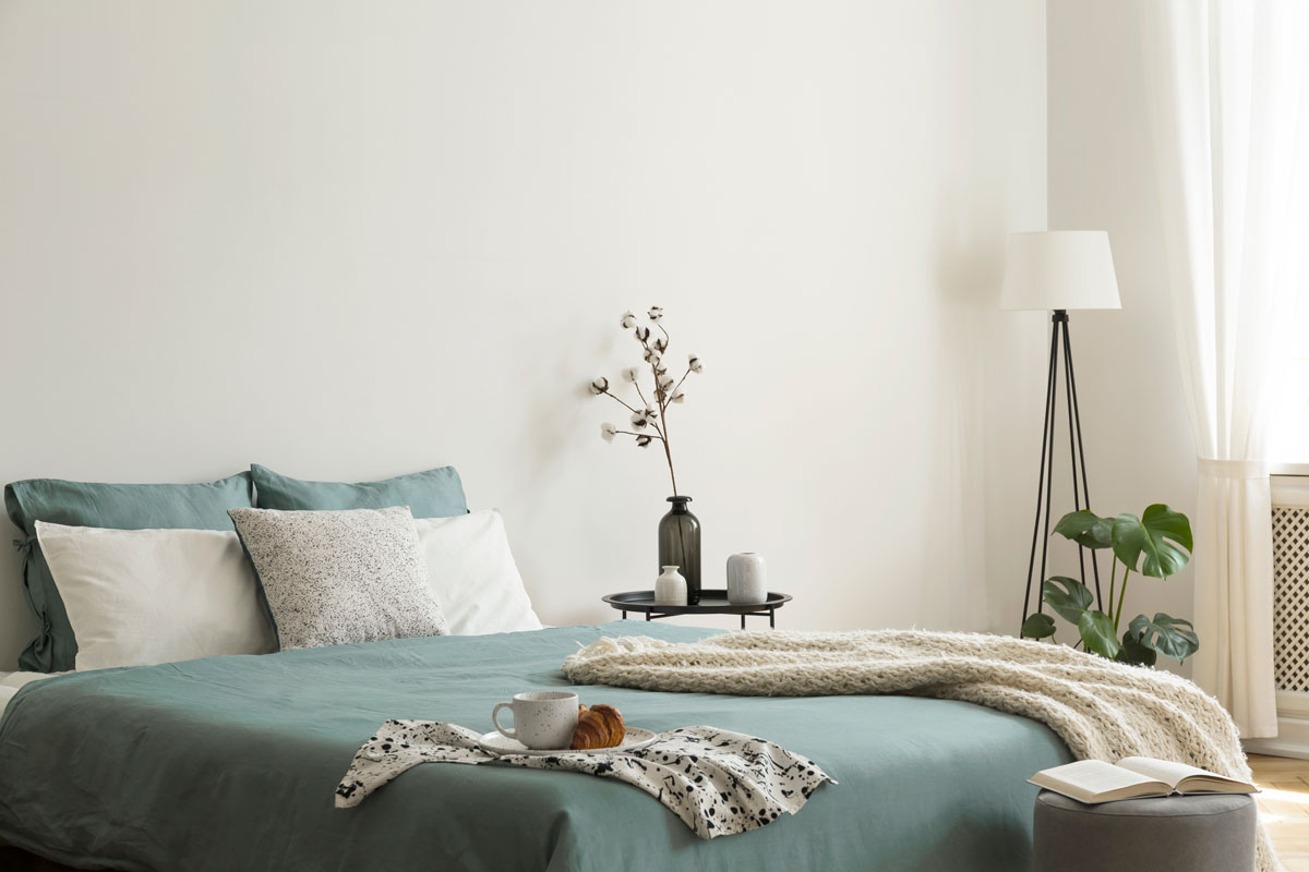 Bedroom interior with sage green and white sheets and cushions and a blanket