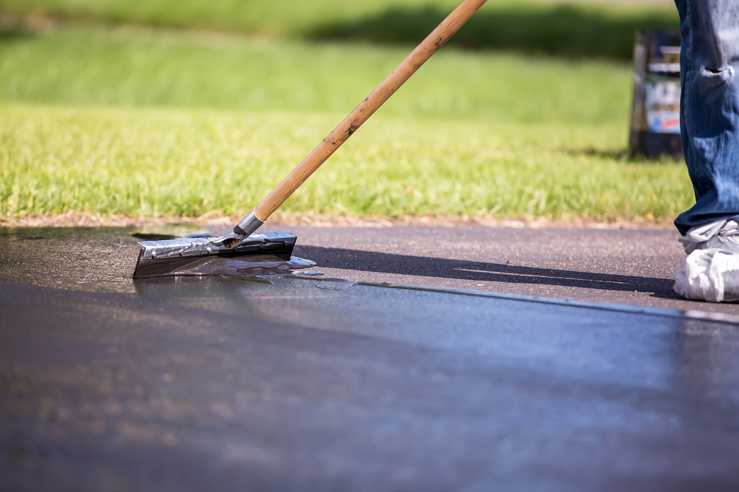 Close-up of a home owner seal coating their own driveway. They are using the "broom" to spread out the sealer on the driveway.