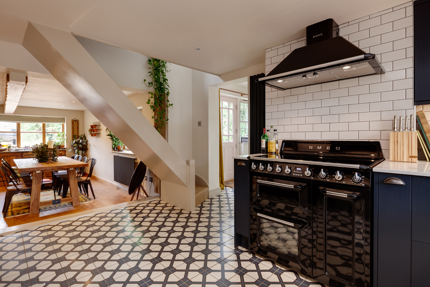 Cottage kitchen with distinctive traditional tile floor and striking dark coloured cabinetry with a range cooker, extractor hood and dining room in view