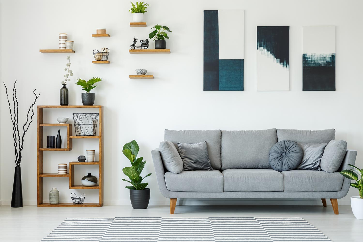 Elegant living room interior with a grey sofa, wooden shelves, plants and paintings on the wall