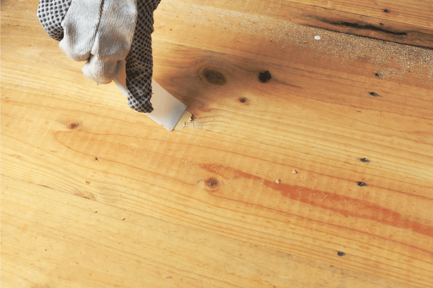 Hand in glove with trowel applying wood filler before sanding