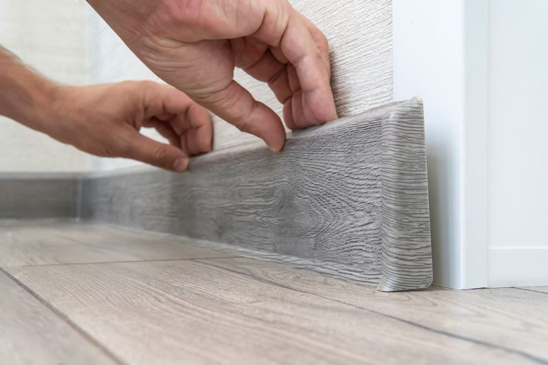 Interior designer properly placing gray PVC baseboard onto the wall, How To Nail Baseboards Without A Nail Gun