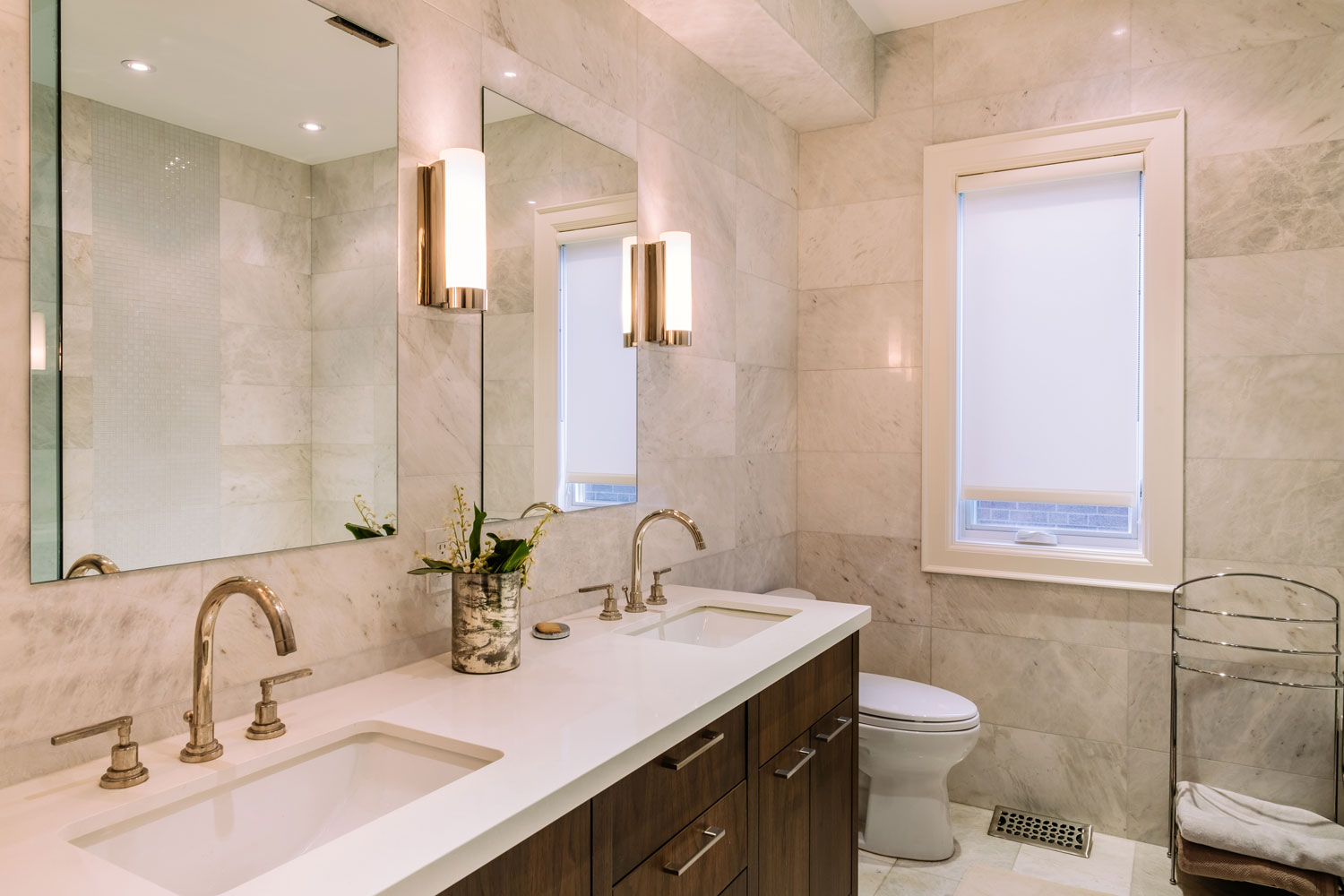 Interior of a gorgeous modern contemporary bathroom with white countertop and gold plated fixtures and wall lamps