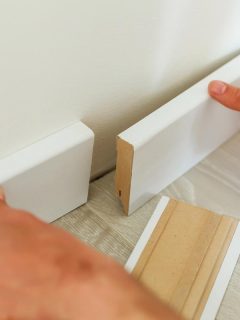 A mans hand putting white baseboard, Should Baseboards Match Wall Or Floor?