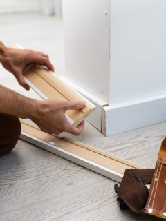 Mans hands putting white baseboard - How To Fix Gaps In Baseboard Corners