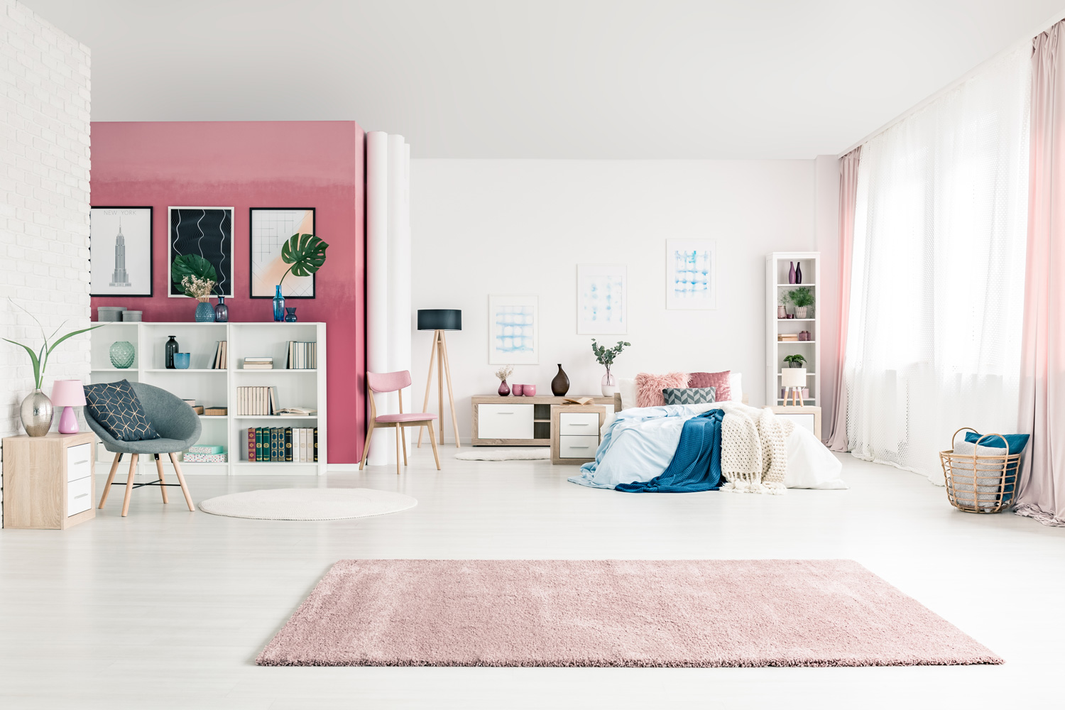 Open space bedroom interior with big rug, cozy bed, pink and white walls, chairs, posters, basket, pink drapes and bookcases