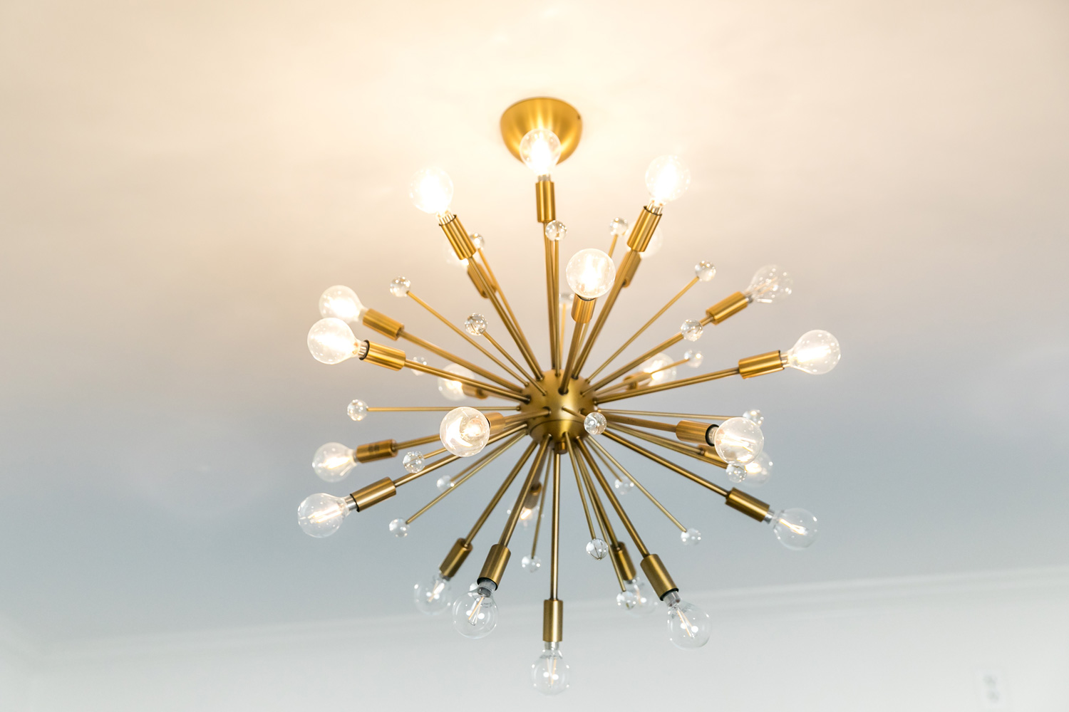 Retro starburst warm gold lighting fixture chandelier against a white wall