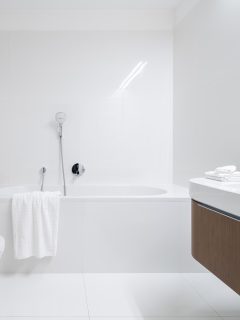 Spacious and elegant bathroom with big bathtub, white tiles, washbasin with wooden cabinet with drawer and big mirror - What To Do With Space At End Of Bathtub [Ideas Explored]