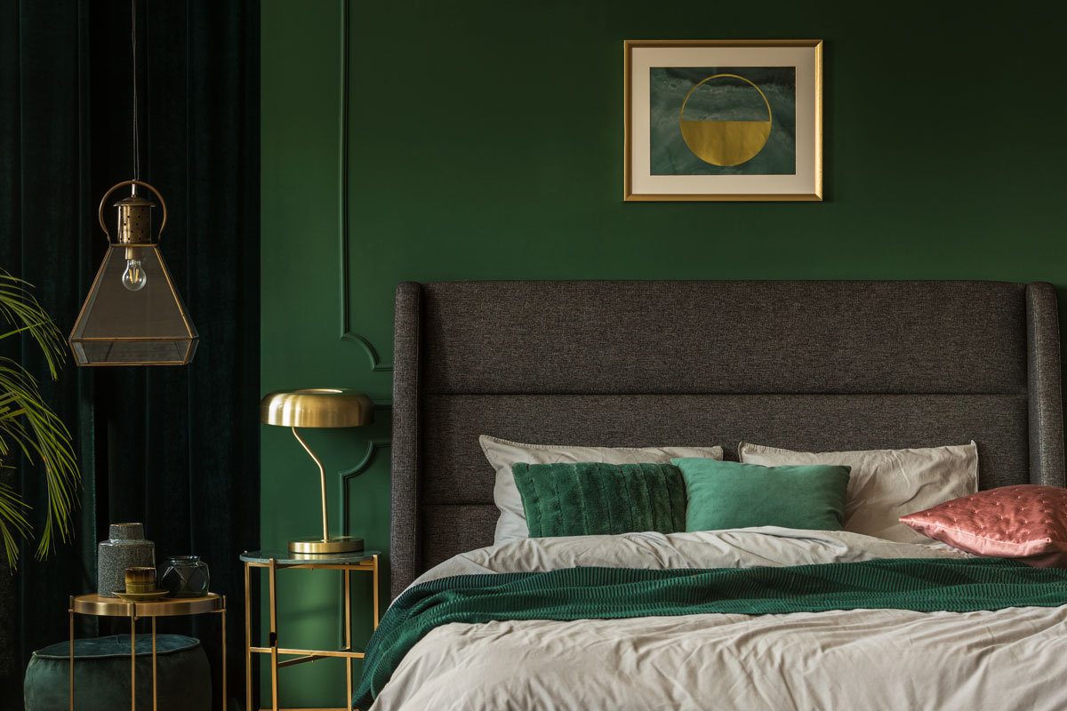Stylish emerald green and golden poster above comfortable king size bed with headboard and pillows in dark green bedroom