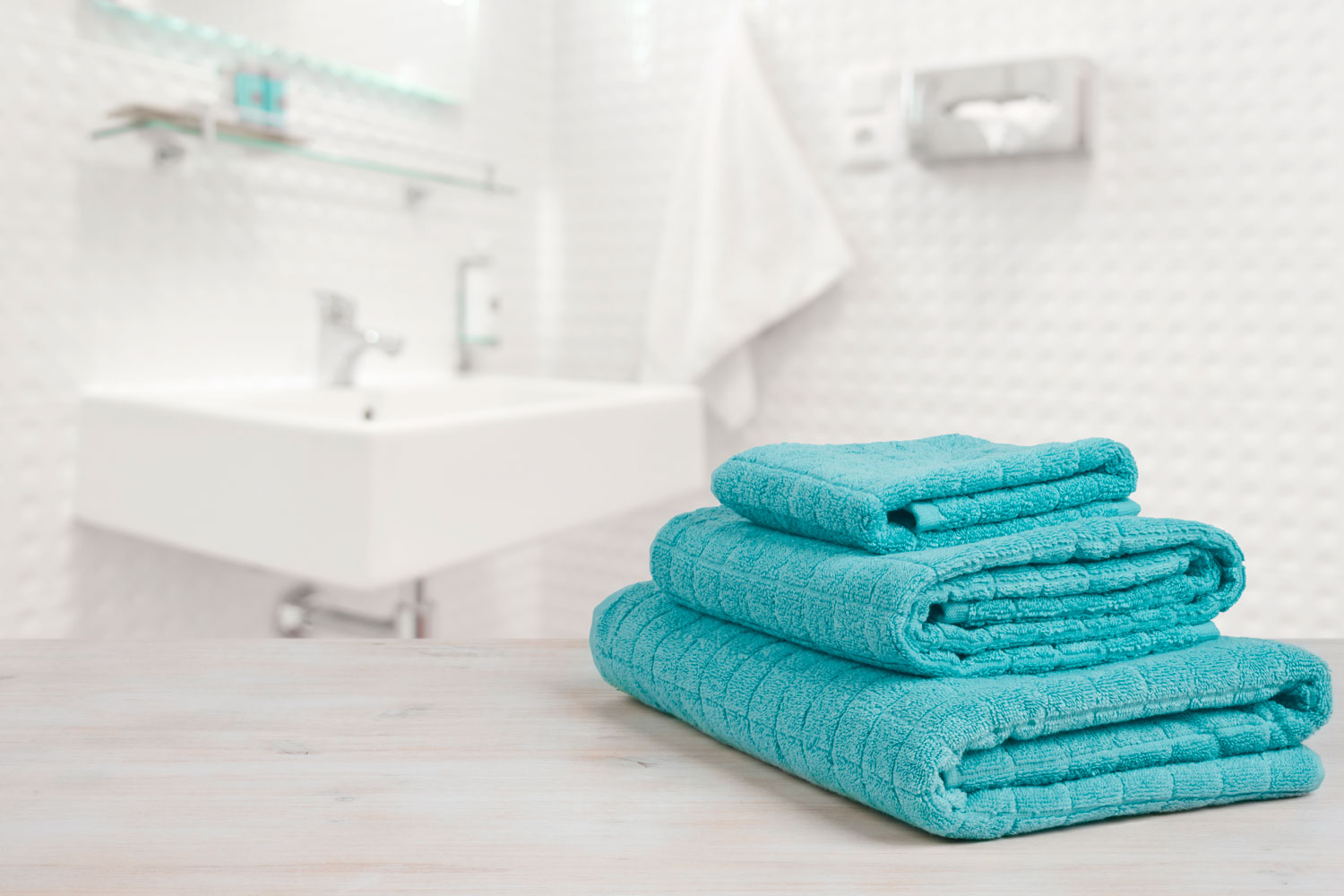 Three different sizes of sky blue colored towels inside a white bathroom