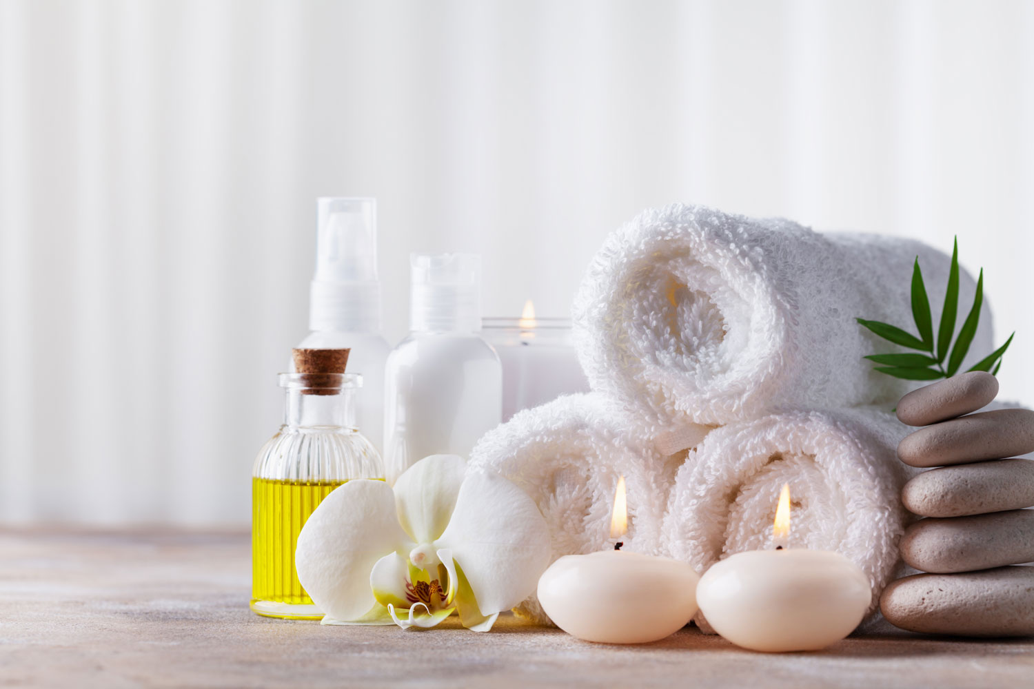 Three white rolled towels with candles on the side and essential oils