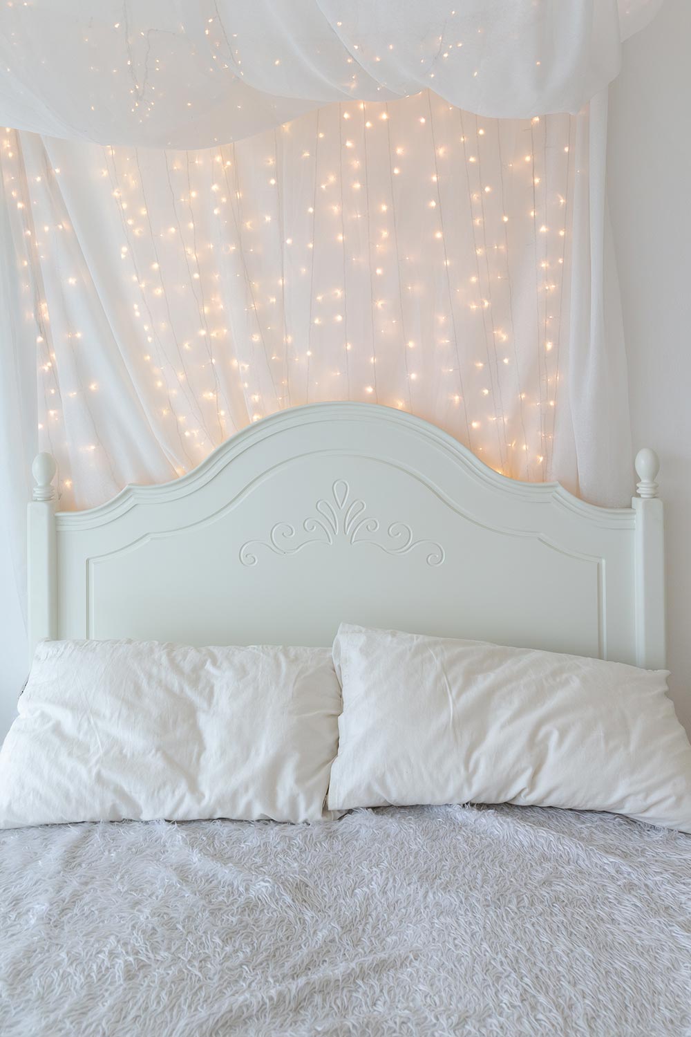 White bed and double pillow covered by messy wool with little orange LED decoration