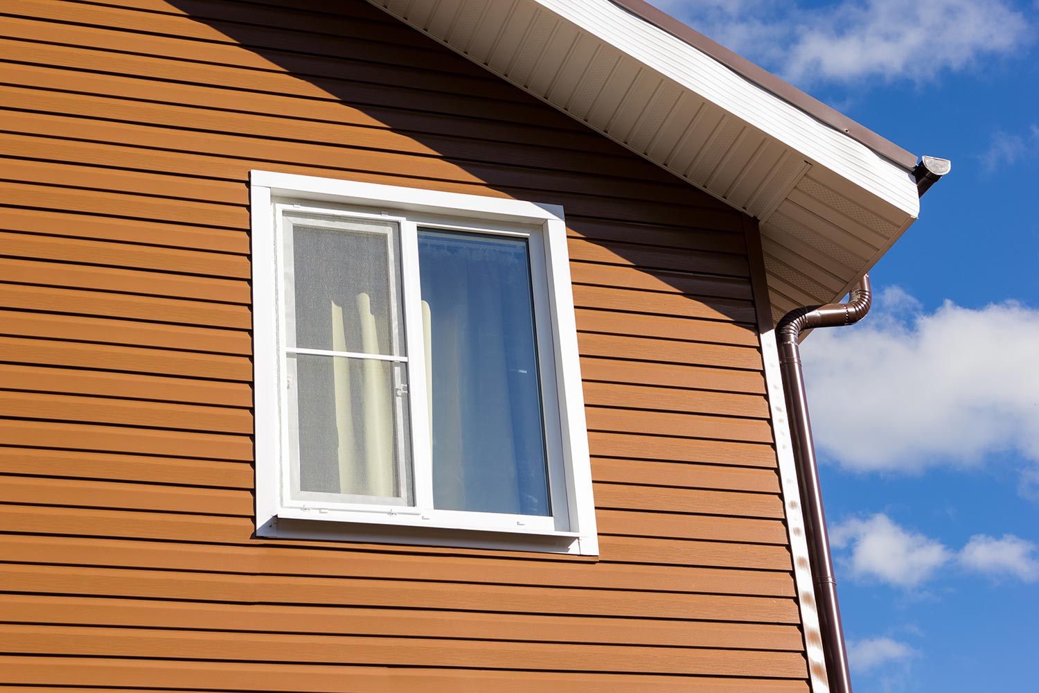 Window in the wall of brown vinyl siding