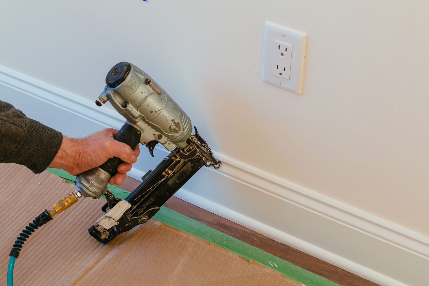 Worker using a brad nail in installing baseboard