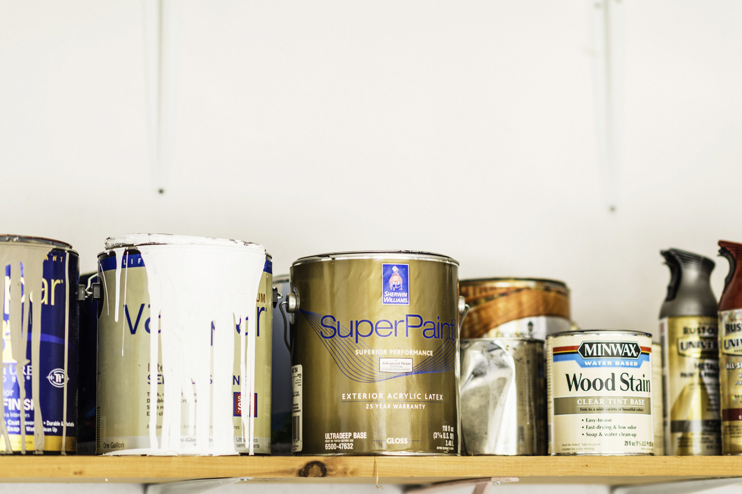  A horizontal shot of a collection of opened and unopened American brand cans of paint, wood stain and paint sprays organized neatly on a wooden shelf