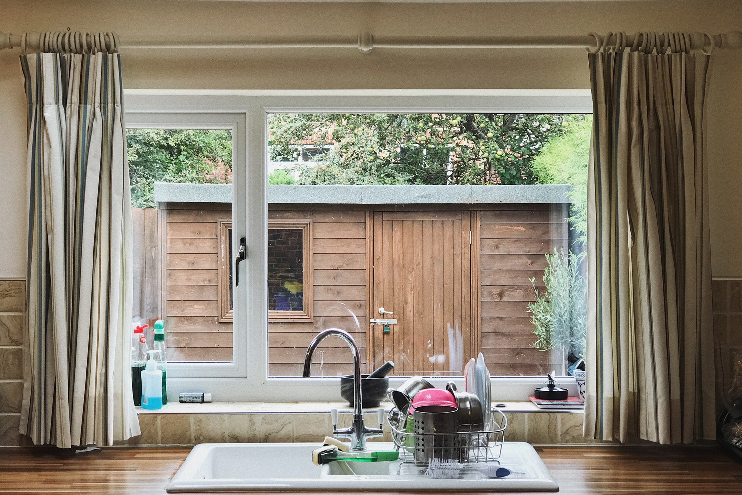 A view through an English kitchen window, the dishes are washed and stacked. A garden shed is visible in the background.