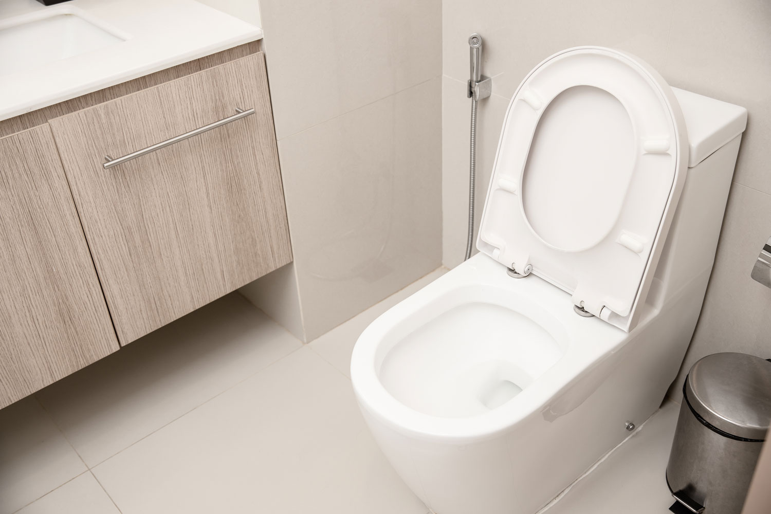 A white toilet to wall type of toilet inside a bright bathroom with a laminated cabinet vanity area