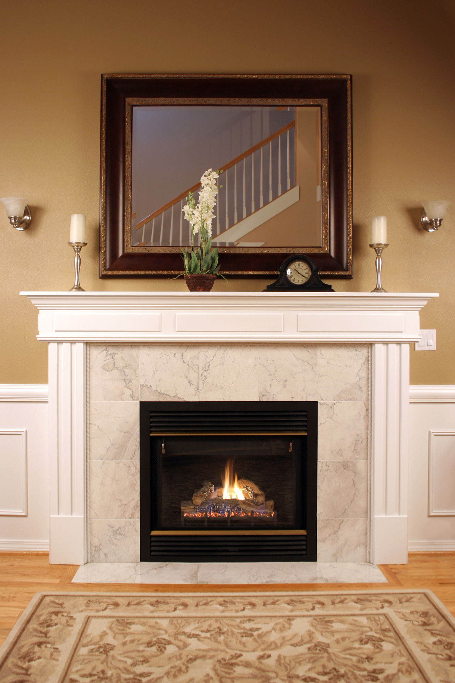 An interior shot of a marble fireplace with beautiful woodwork,a framed mirror and warm inviting colors.