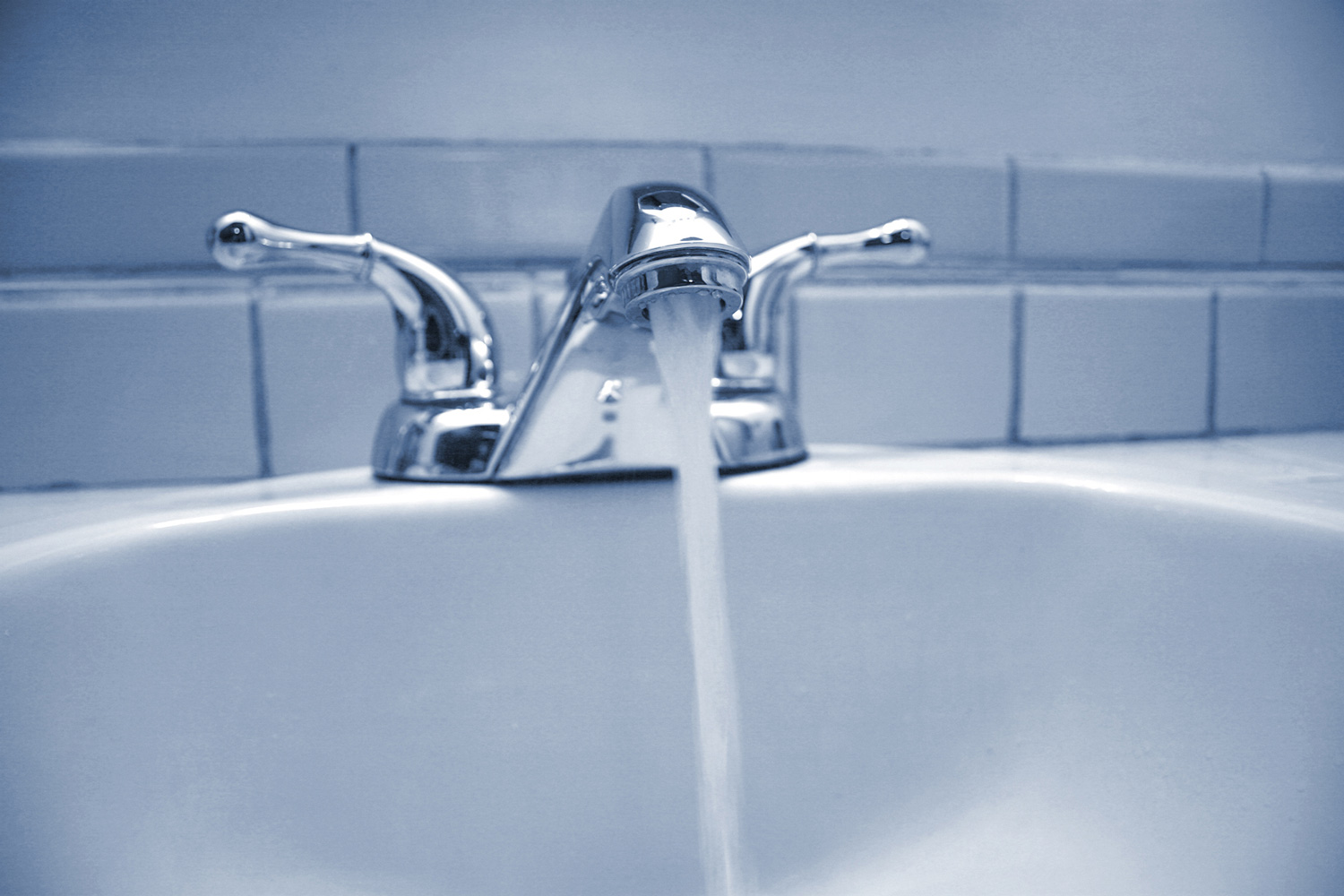 Blue filtered image of a bathroom sink with water running.