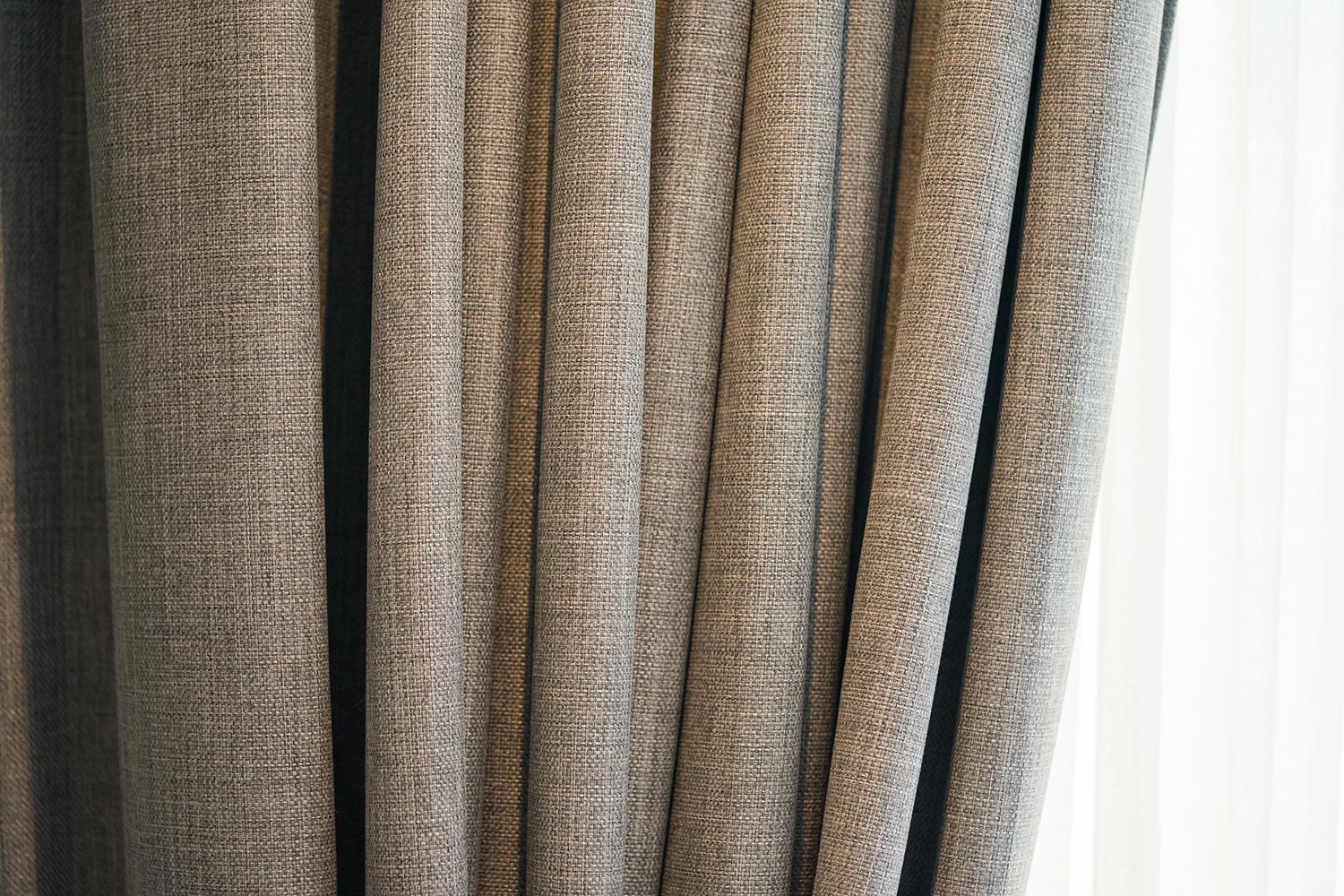 Bright curtain in thin and thick vertical folds made of dense fabric