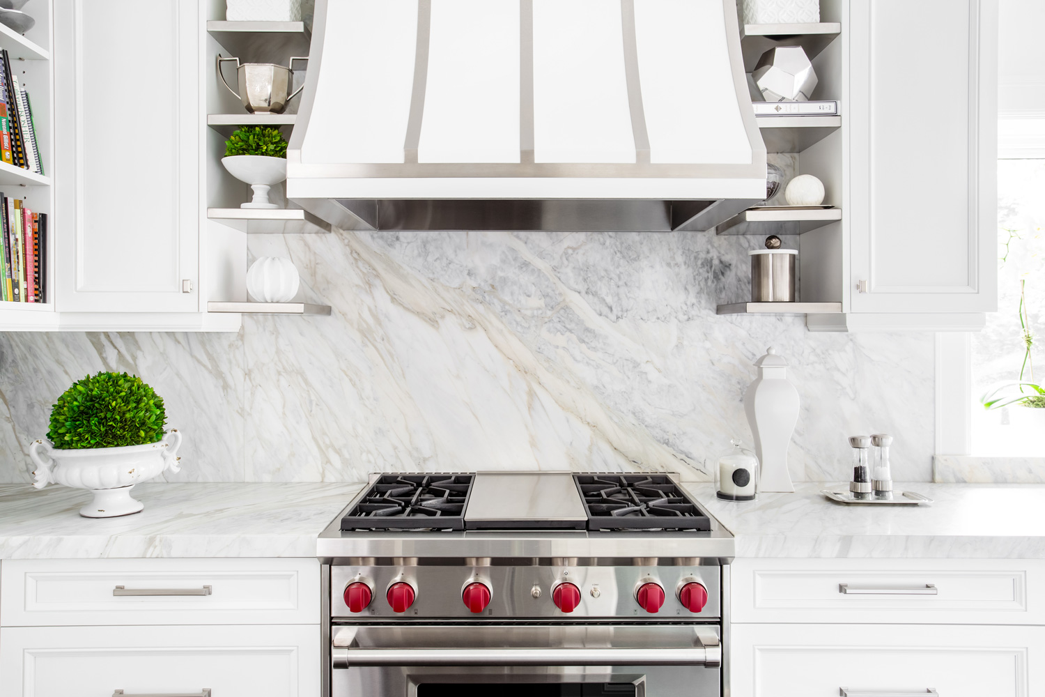 Bright horizontal image of classic white kitchen, with gas range and marble backsplash.