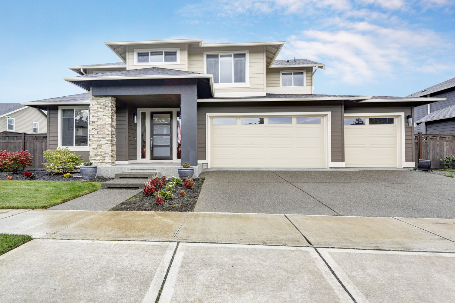 Curb appeal of brand-new home in brown and beige colors with two garages and concrete driveway.
