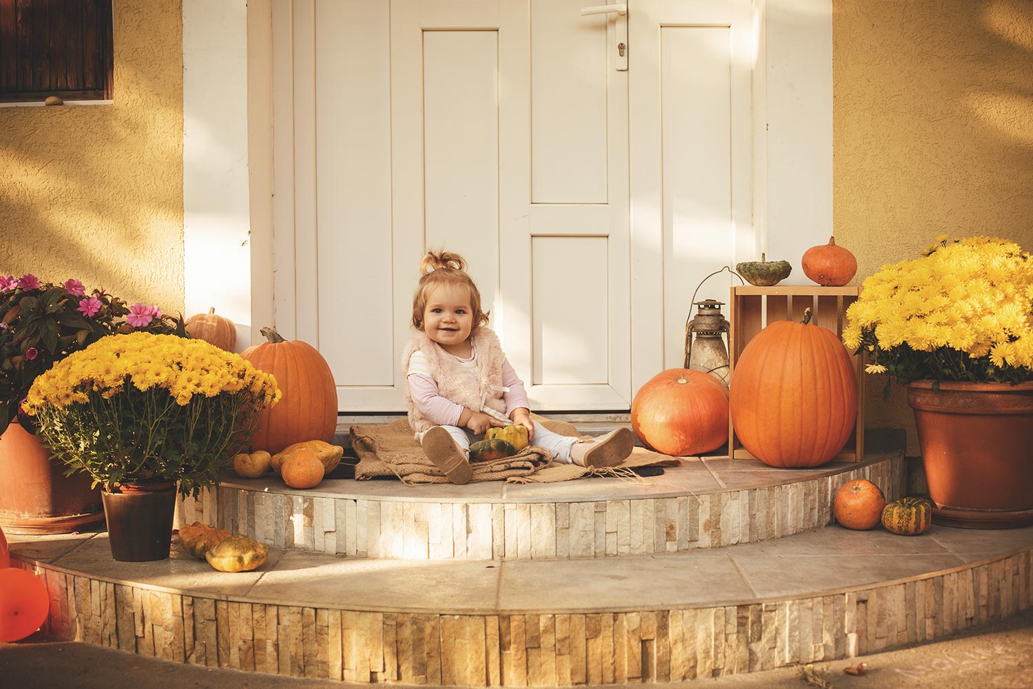 Happy baby girl is sitting on front porch on a beautiful autumn day