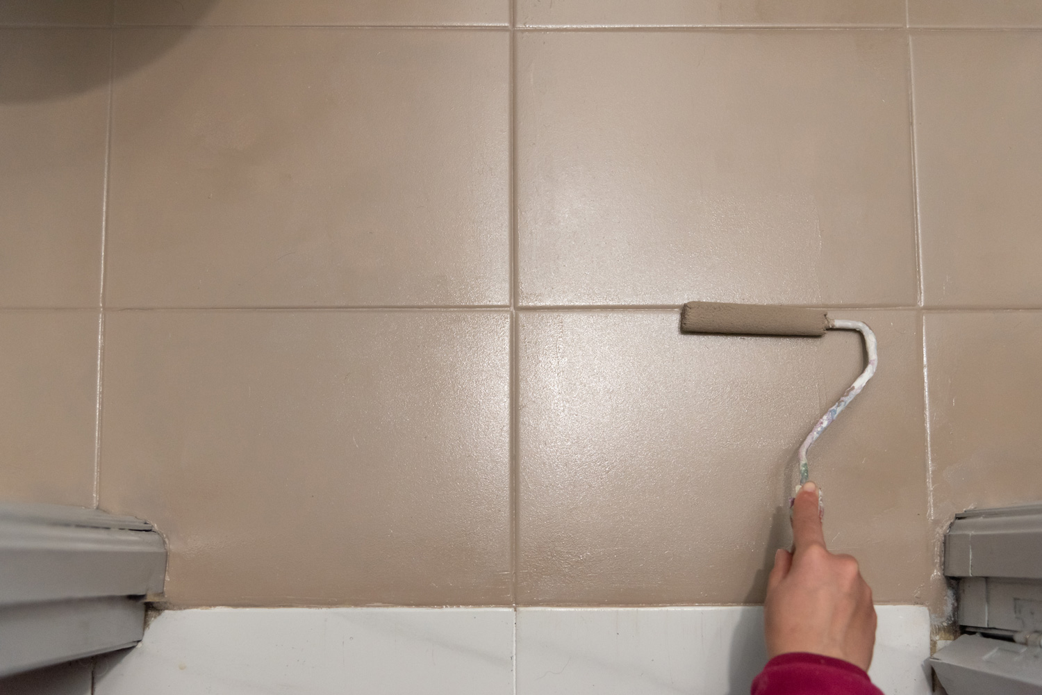 Human-hand-holding-paint-roller-over-floor-tile-in-the-bathroom-as-restyling-home-decoration-and-doing-cheap-maintenance.