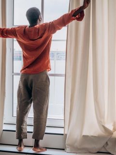 A man stretches after waking up standing at the window, Curtain Length Rules You Should Know [By Type Of Window]
