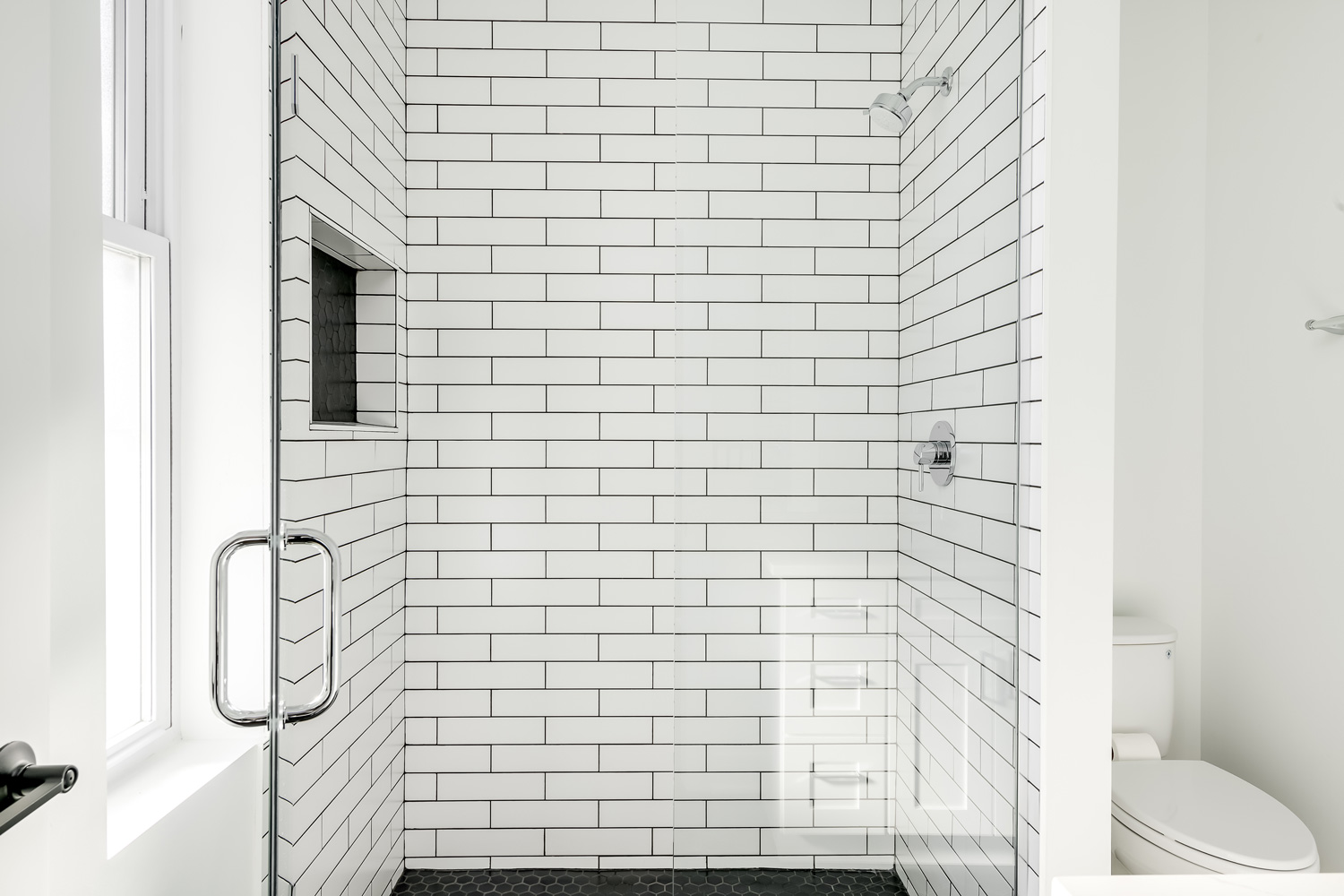 Modern All White Bathroom with White Subway Tile in Shower and Black Hexagon Tile on the Floor