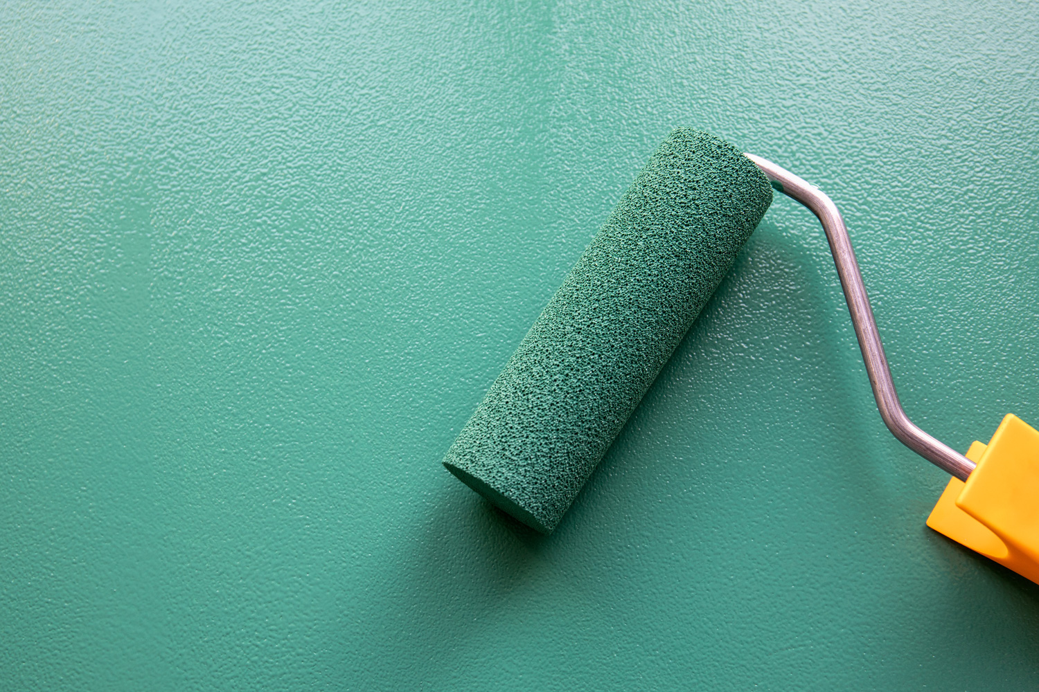 Paint roller with green colour on painted wooden surface. Chalk board. Painting and renovation.