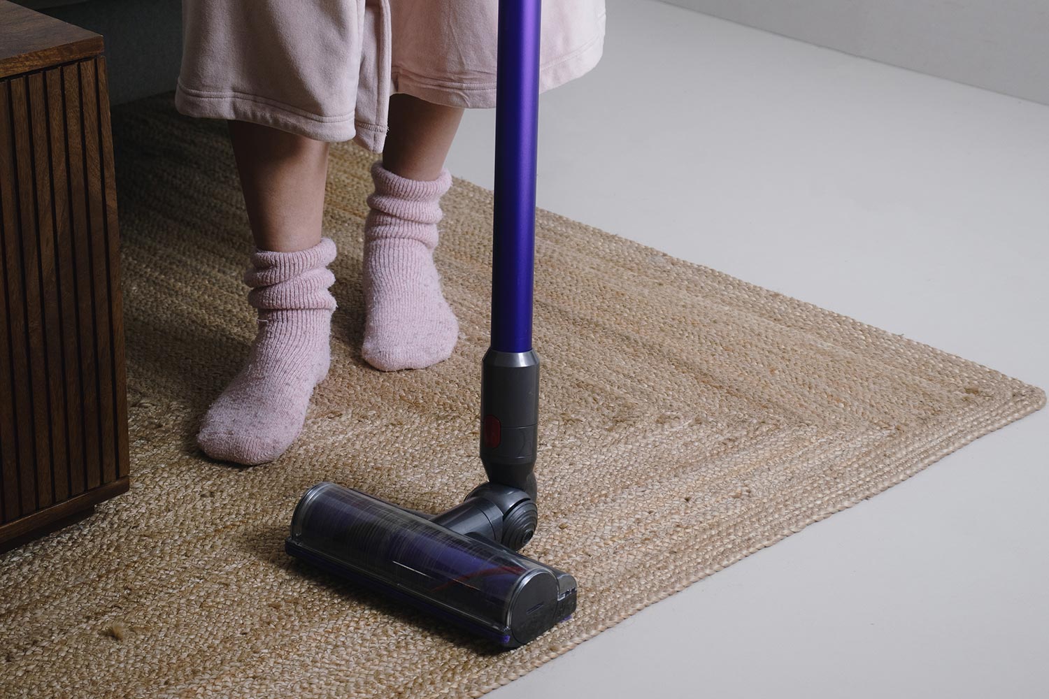 The girl cleans the flooring in the room with a hand vacuum cleaner