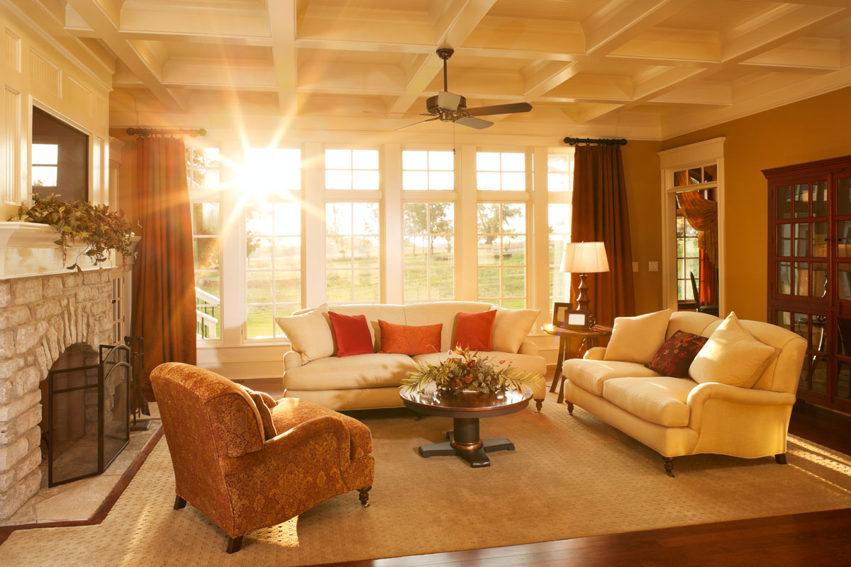 Warm afternoon sunlight pours into an elegant home's living room with a stone fireplace and large windows
