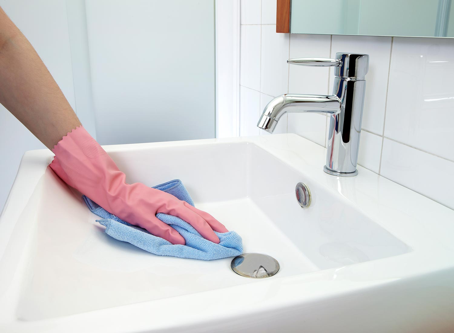 Woman cleaning the washbasin with microfiber cloth and glove