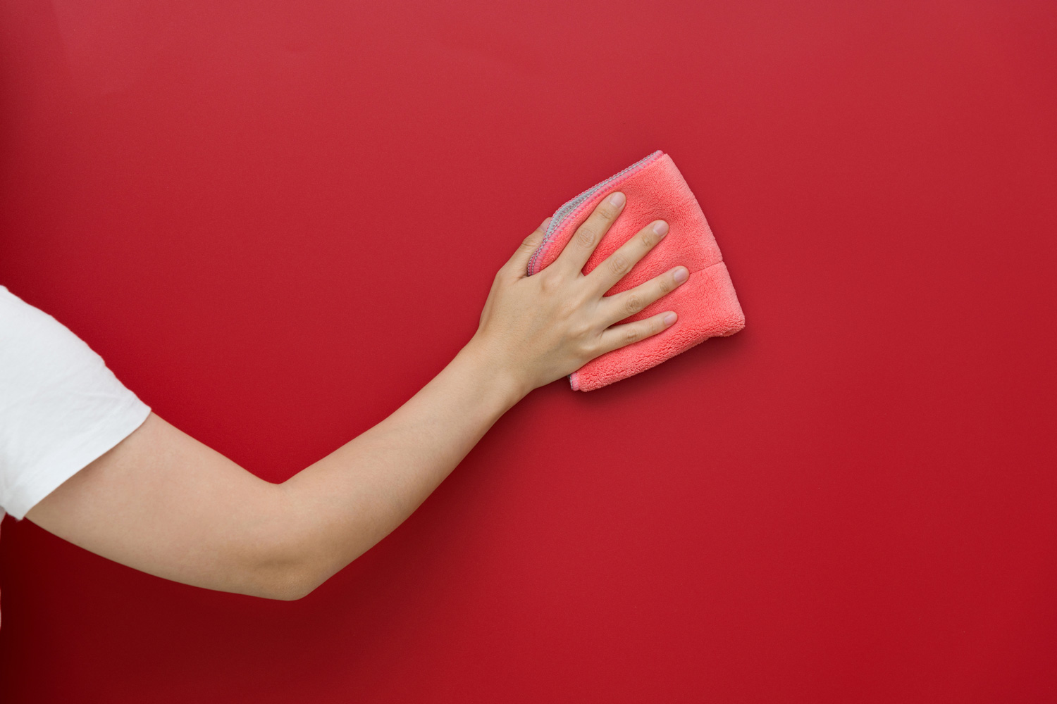 Woman hand cleaning red wall with rag.