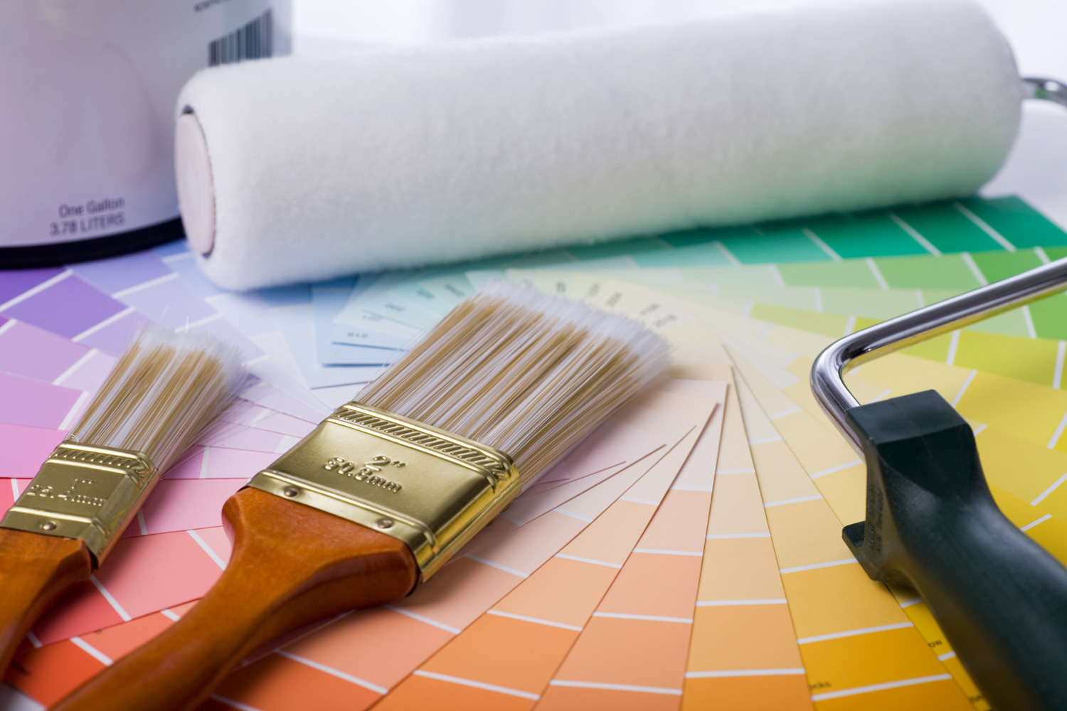 close-up image of paint brushes, roller, paint can, and paint samples