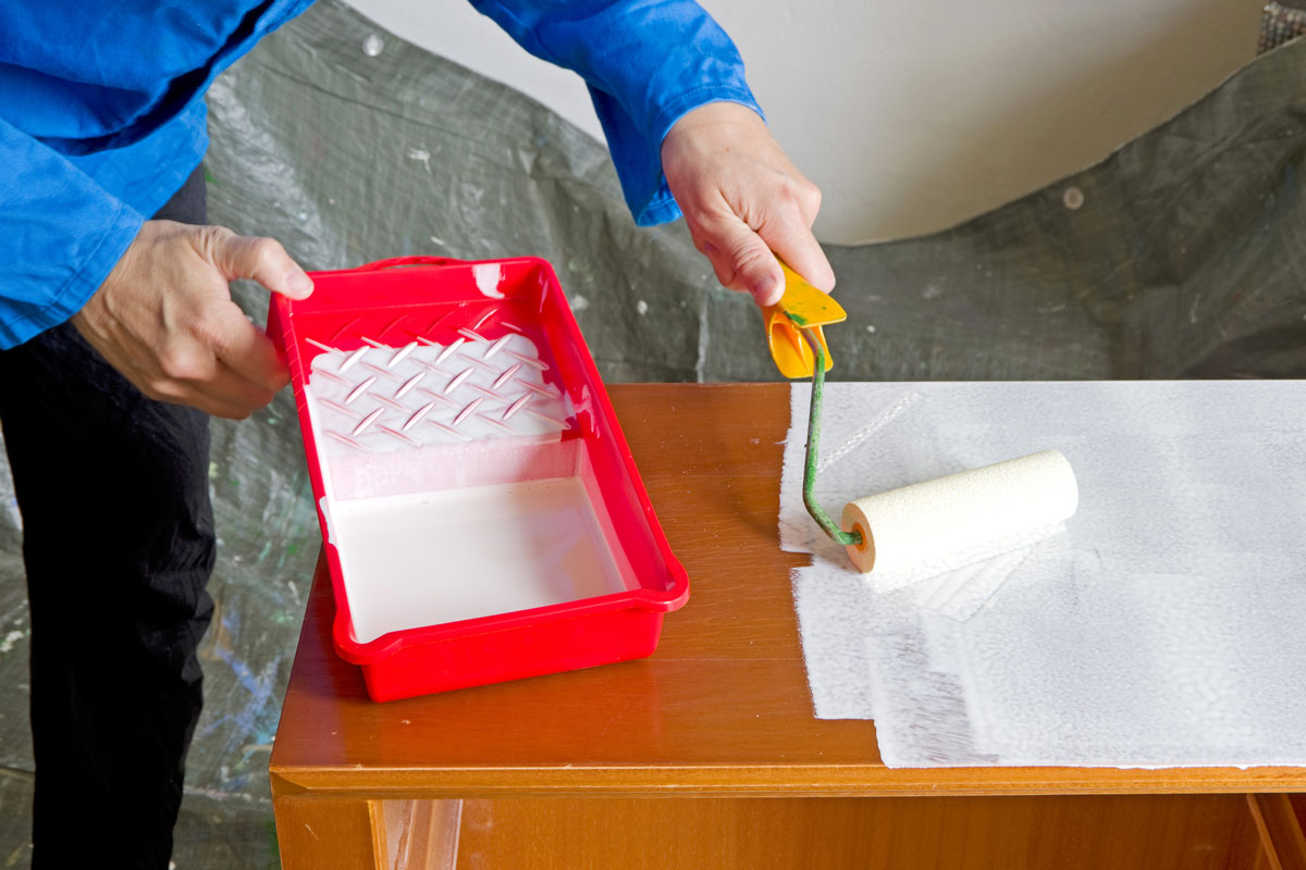 painter with paint roller painting a wooden cabinet