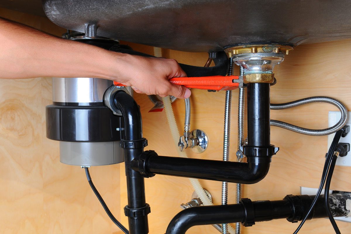 plumber using a wrench to tighten a fitting beneath a kitchen sink