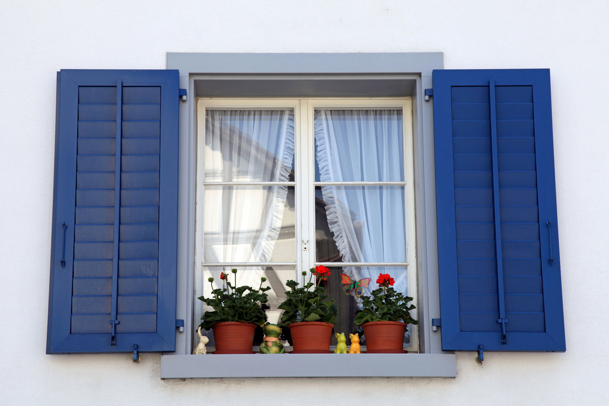 rustic window with blue shutters and flower pots in white rural house