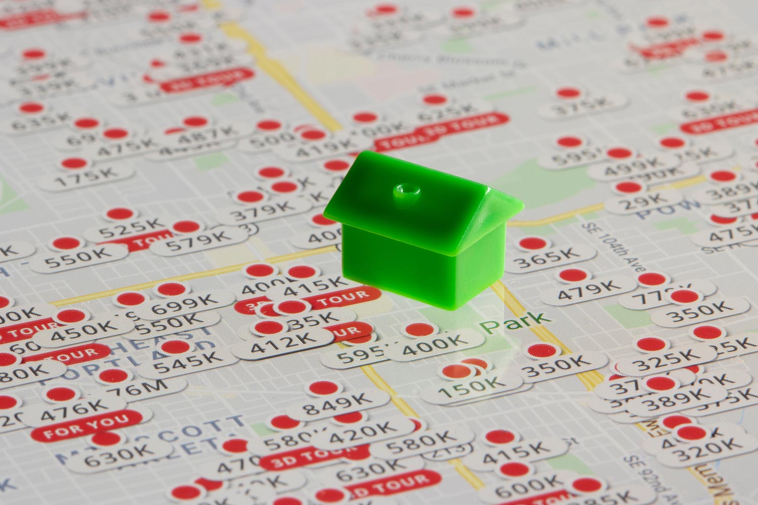 A green plastic toy house sits on top of the Zillow website's map page showing listed properties in Portland