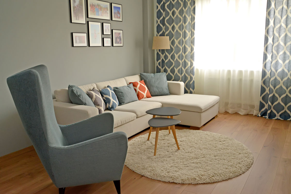 A light blue accent chair with beige sofas and patterned throw pillows inside a contemporary inspired living room