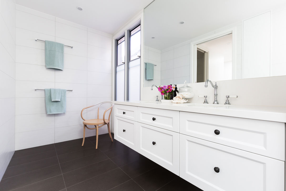 A long white vanity with white countertop inside a narrow bathroom with white walls