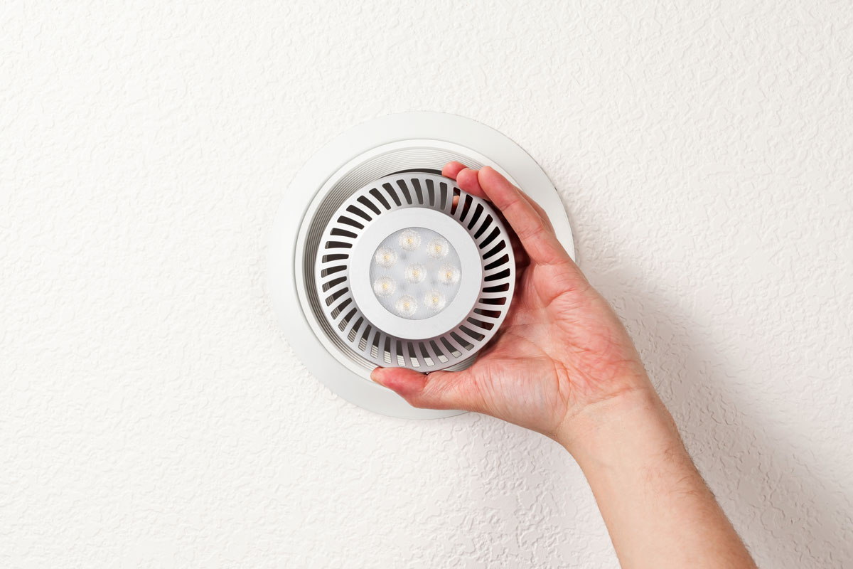 A male hand is installing an energy efficient LED light bulb into a ceiling can fixture