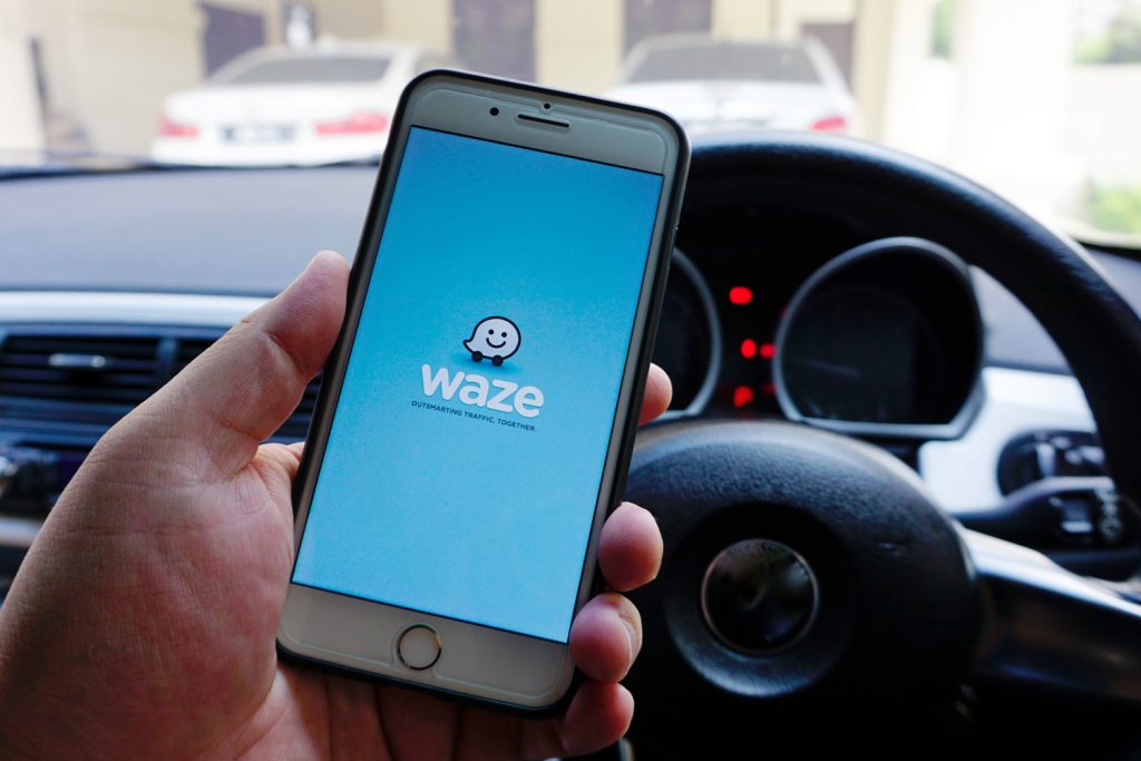 A man holding the iPhone 7 Plus with Waze navigation app inside the car. 