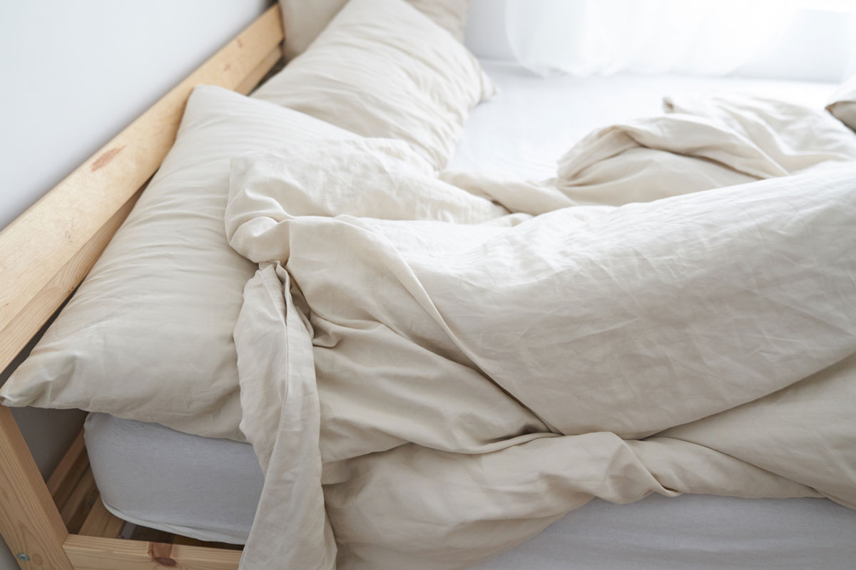 A messy bed with a beige color of blanket and bed sheet