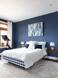A navy blue bedroom with wood framed windows a bed sitting on a rug and hardwood floors, and a Peloton - What Colors Go With Navy Blue