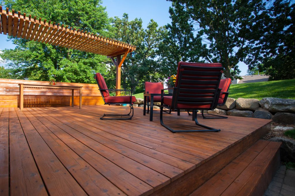 Backyard deck with deck chairs and a pergola on a sunny summer day.