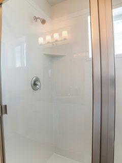 Bathroom interior of a shower stall with glass and stainless steel. There is a white door, wall mounted shower head inside and a window - Can You Paint A Fiberglass Shower [And How To]